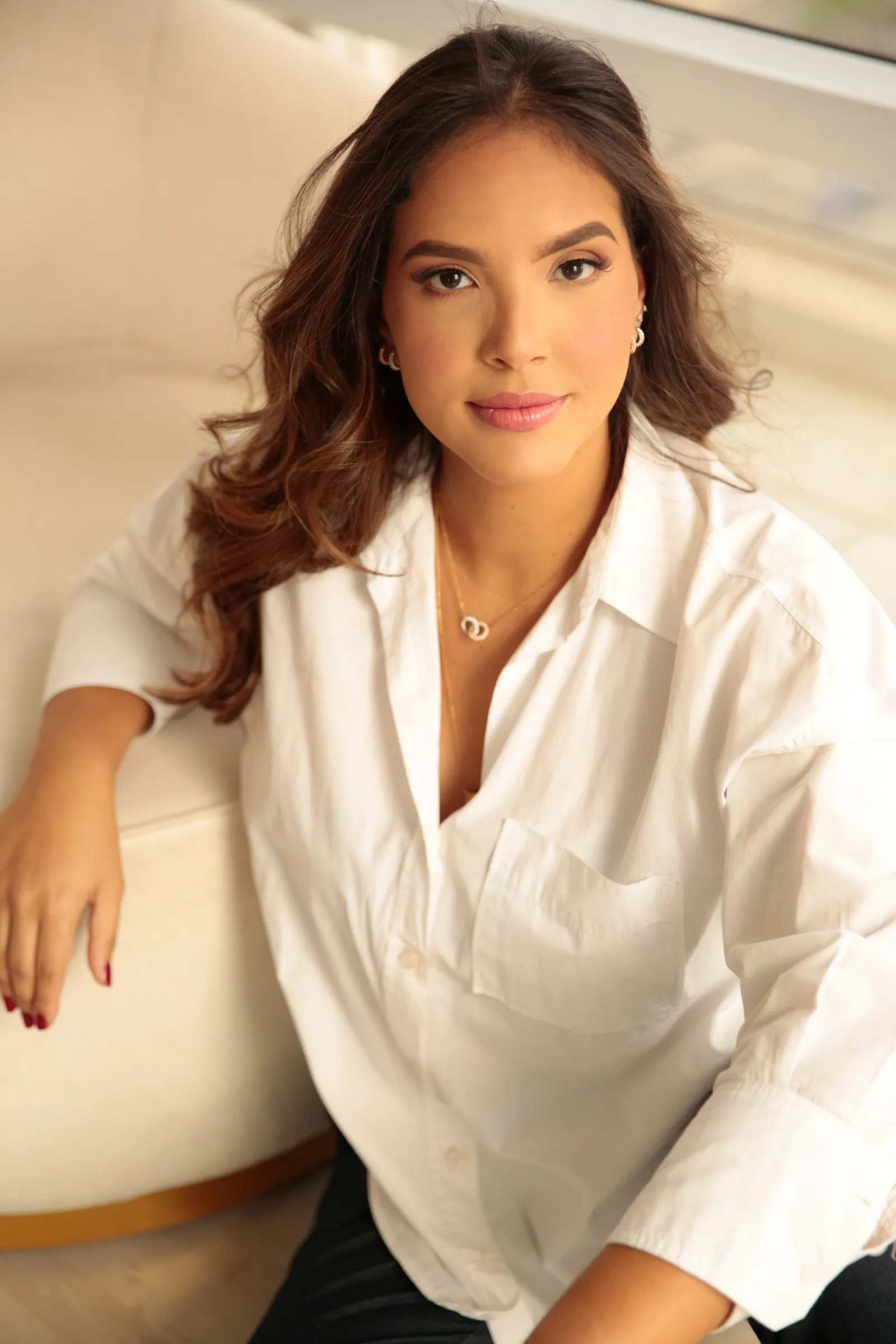 Dra. Gabriela Gomes sentada, de camisa branca, olhando para a câmera